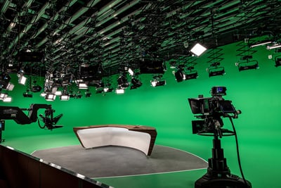 Fernsehstudio mit grünem Hintergrund, Kameras und Beleuchtung.