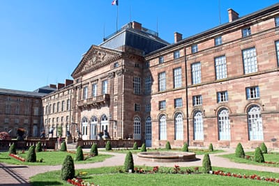Historisches Gebäude mit gepflegtem Garten und Springbrunnen.