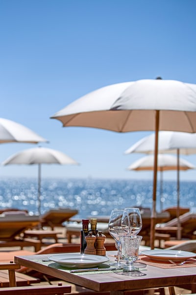 Tisch mit Geschirr und Gläsern unter Sonnenschirmen am Meer.