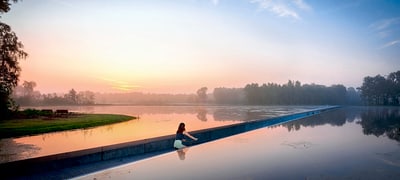 Person sitzt am Rand eines Sees bei Sonnenaufgang.