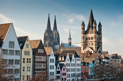 Bunte Häuserzeile und Dom in Köln bei Tageslicht.
