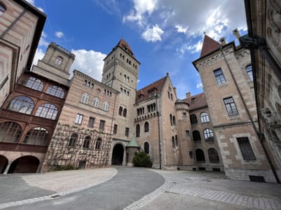 Innenhof eines historischen Gebäudes mit Türmen und blauem Himmel.