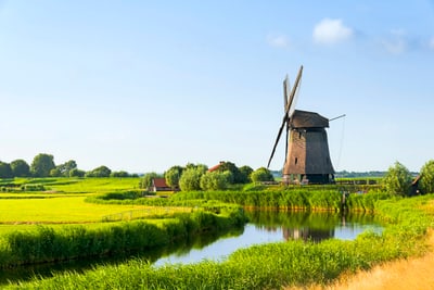 Windmühle in grüner Landschaft neben einem Fluss.