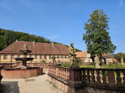 Historische Gebäude mit Statuen und Bäumen im Vordergrund an einem sonnigen Tag.