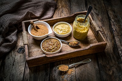 Ein Holztablett mit verschiedenen Senfsorten in Schalen und Gläsern auf einem Holztisch.