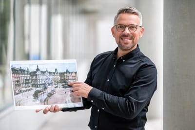 Mann in schwarzem Hemd hält ein Bild in einem Korridor.