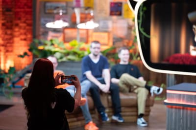 Person macht ein Foto von zwei sitzenden Personen in einem Studio.