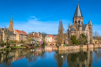 Fluss mit historischer Kirche und Gebäuden im Hintergrund, blauer Himmel.