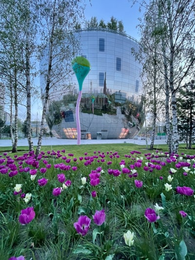 Spiegelndes Gebäude hinter blühendem Blumenbeet mit Bäumen.