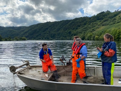 Menschen in orangefarbenen Overalls auf einem Boot auf einem See.
