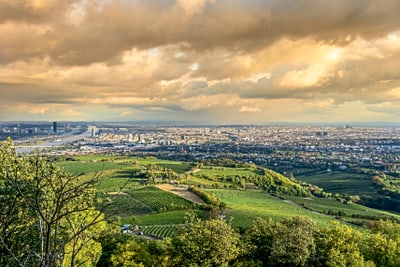 Panoramablick auf eine Stadt mit grünen Hügeln und dramatischem Himmel.
