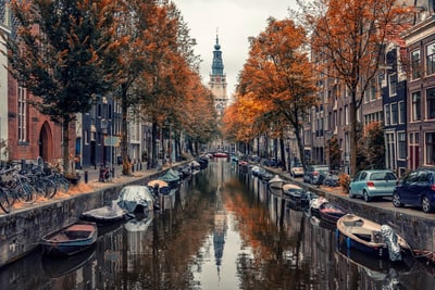 Herbstlicher Kanal in Amsterdam mit Booten und Bäumen.