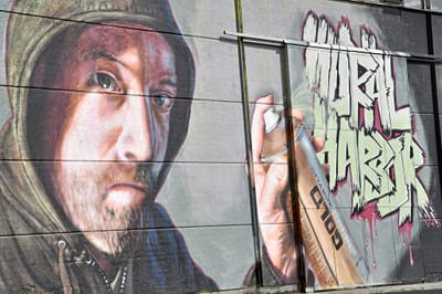 Wandgemälde mit einem Mann in einem Kapuzenpullover und Graffiti-Schriftzug.