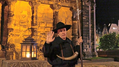 Nachtwächter vor beleuchteter historischer Fassade mit Laterne.