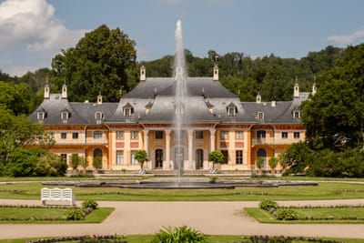 Grosses barockes Gebäude mit Brunnen und Garten im Vordergrund.
