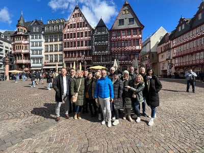 Gruppe von Menschen auf einem Kopfsteinpflasterplatz vor Fachwerkhäusern.