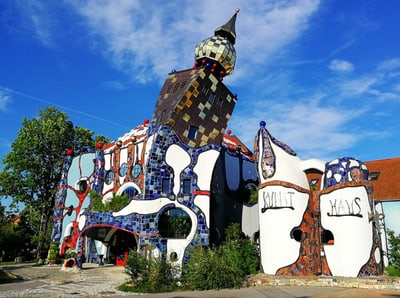 Buntes Gebäude mit asymmetrischem Design und Turm vor blauem Himmel.