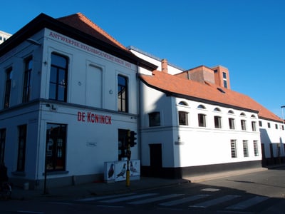 Weisses Gebäude mit rotem Dach an einer Strassenecke bei blauem Himmel.