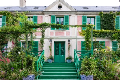 Fassade eines Hauses mit grünen Fensterläden und Pflanzen, die die Fassade schmücken.