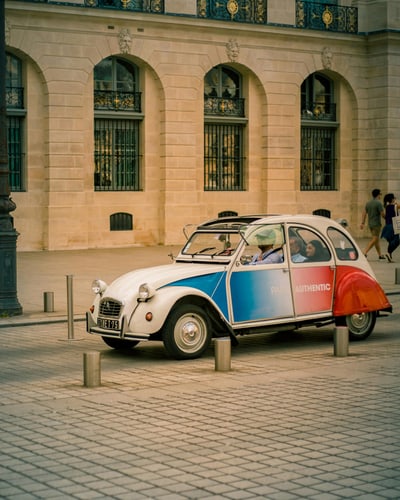 Bunter Citroën 2CV auf Kopfsteinpflaster vor historischem Gebäude.