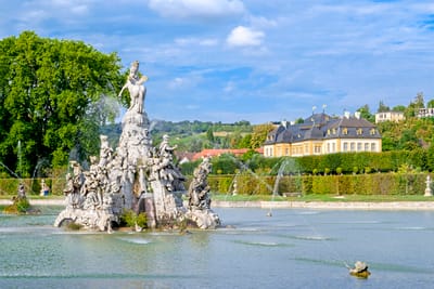 Prunkvoller Springbrunnen im Park mit Schloss und blauem Himmel.