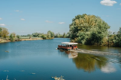 Boot fährt auf ruhigem Fluss mit Bäumen am Ufer.