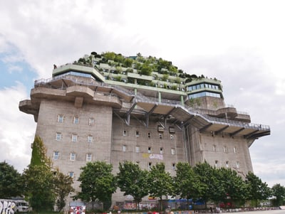 Grosser grauer Bunker mit begrüntem Dach und Terrasse, Bäume im Vordergrund.