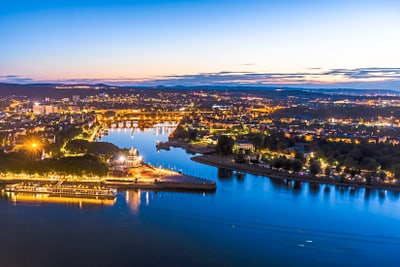 Stadtansicht bei Dämmerung mit Fluss und beleuchteten Gebäuden.