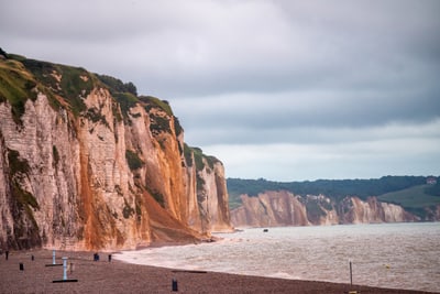 Steilküste am Meer mit wolkigem Himmel und Kiesstrand.