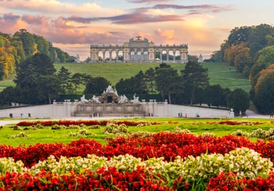 Garten mit roten Blumen, im Hintergrund ein historisches Bauwerk auf einem Hügel.