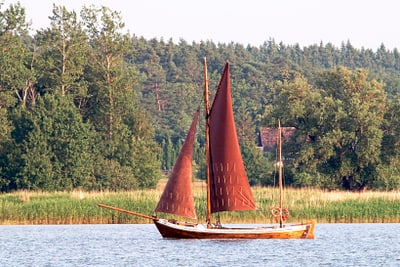 Segelboot auf einem See vor bewaldeter Kulisse.