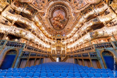 Prunkvolles Opernhaus mit dekorativer Decke und blauen Sitzreihen.