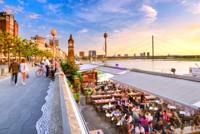 Flussuferpromenade in Düsseldorf mit Rhein, Fernsehturm und Cafés.