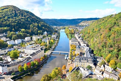 Panoramablick auf Fluss und Stadt zwischen bewaldeten Hügeln.