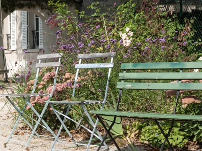 Metallstühle vor blühenden Sträuchern im Garten.