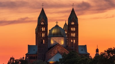 Majestätische Kathedrale bei Sonnenuntergang mit drei Türmen vor orangefarbenem Himmel.