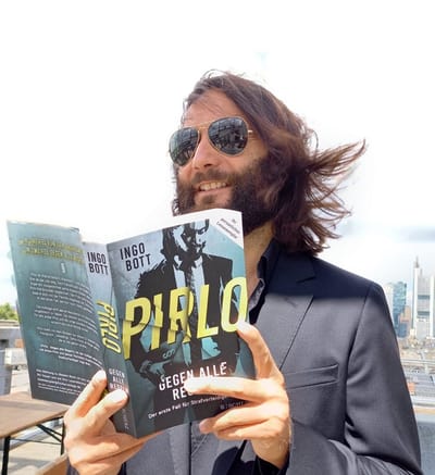 Person mit Sonnenbrille liest Buch auf einer Dachterrasse.