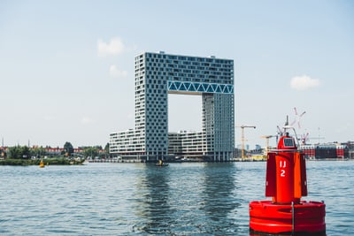 Moderne Architekturgebäude mit rechteckigem Durchgang am Wasser, Boje im Vordergrund.