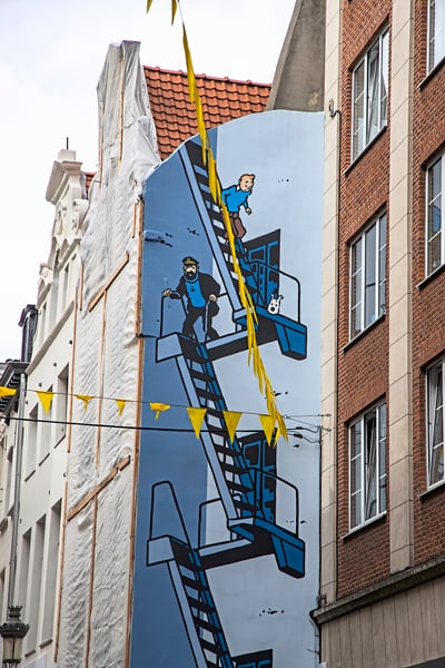 Wandgemälde auf einem Gebäude mit zwei Comicfiguren auf einer Treppe.
