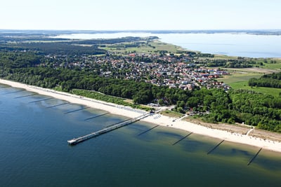 Luftaufnahme einer Küstenstadt mit Strand, Wald und Pier.