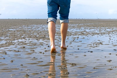 Person geht barfuss im flachen Wasser am Strand.