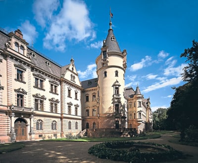 Historisches Schloss mit Türmen und dekorativer Fassade unter blauem Himmel.
