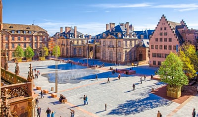 Historischer Platz mit alten Gebäuden und Menschen in sonnigem Wetter.