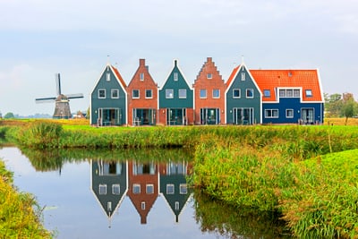 Reihenhäuser und Windmühle am Kanal in grüner Landschaft.