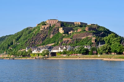 Festung auf grünem Hügel am Flussufer.