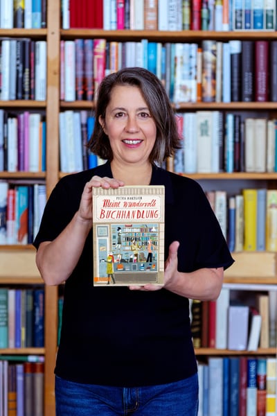 Person hält ein Buch vor einem Bücherregal.
