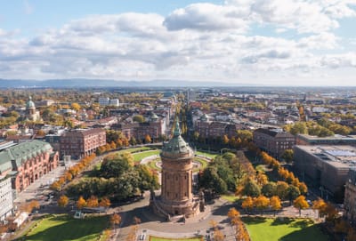Luftaufnahme eines historischen Turms in einem Stadtzentrum mit umliegenden Parks und Gebäuden.