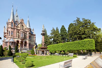 Historisches Schloss mit Garten und Statue bei klarem Himmel.