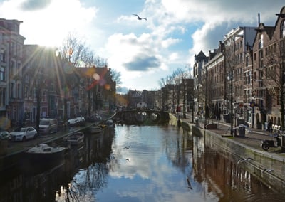 Sonniger Kanal mit Brücke und Gebäuden in Amsterdam.