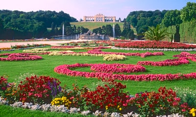 Gartenlandschaft mit Blumenbeeten und historischem Gebäude im Hintergrund.